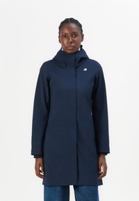 Manteau imperméable bleu marine avec un col montant, des manches longues et un logo sur la poitrine. Présente une silhouette droite et une texture lisse.