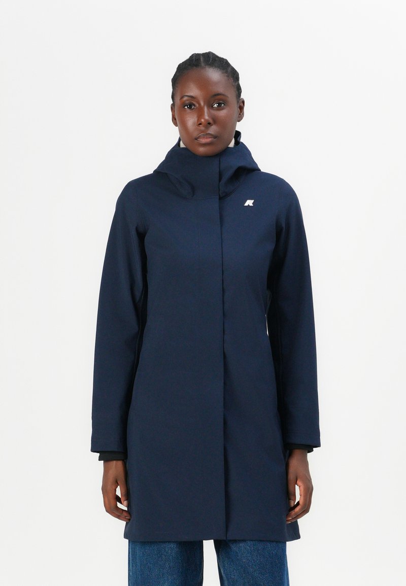 Manteau imperméable bleu marine avec un col montant, des manches longues et un logo sur la poitrine. Présente une silhouette droite et une texture lisse.