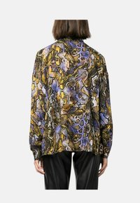 Blusa a maniche lunghe in stampa pitone viola, gialla e nera. Presenta una vestibilità rilassata, un tessuto strutturato e polsini abbottonati sulle maniche.