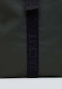 Borsa nera in nylon con una prominente tracolla in tessuto con la scritta "JACKIT" in rilievo. Texture liscia con una leggera lucentezza, forma rettangolare.