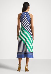 Halternek kjole med vertikale marineblå og hvite striper, med grønne og hvite diagonale detaljer, avsluttet med en blå kant og gullfarget beslag.