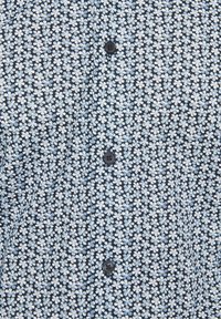 Tissu à motifs floraux bleu et blanc avec quatre boutons bleu foncé alignés verticalement au centre.