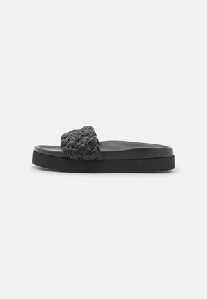 Mule noire avec un dessus tressé, une texture lisse et une semelle plateforme épaisse pour plus de hauteur et de confort.