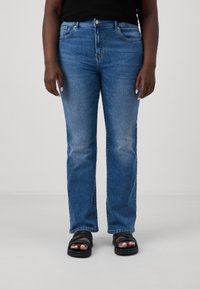 Blå raka jeans med en urblekt design, femfickorsstil och klassisk dragkedja, i kombination med svarta slip-in sandaler.