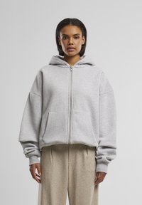 Grau gefütterter Hoodie mit einer großen Kapuze, heruntergezogenen Schultern und zwei Fronttaschen. Weicher Stoff und gerippte Säume sorgen für Textur und einen gelungenen Abschluss.
