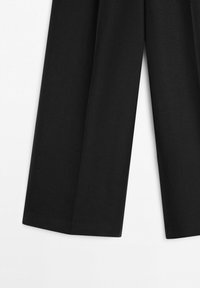 Pantaloni neri a gamba larga con orlo dritto, distesi su uno sfondo bianco, che mostrano la trama del tessuto e le pieghe sartoriali.