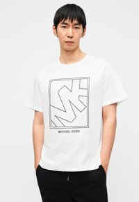 Λευκό βαμβακερό t-shirt με μαύρο γραφικό σχέδιο και το κείμενο «MICHAEL KORS» από κάτω. Κοντά μανίκια και άνετη εφαρμογή.