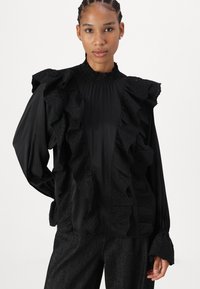 Blusa negra con acentos de encaje con volantes. Presenta un cuello alto, mangas largas y un detallado intrincado a lo largo del frente y las mangas.
