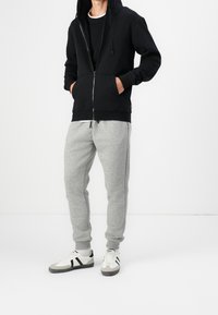 Sudadera negra con cremallera y capucha, combinada con pantalones de chándal gris claro y zapatillas que presentan detalles en blanco y negro.