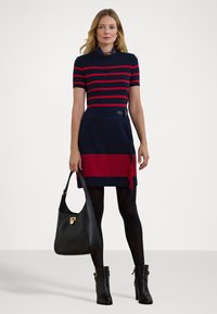 Pleteni top s crvenim i mornarsko plavim prugama, kratki rukavi; mornarsko plava suknja s crvenom horizontalnom trakom i detaljima od franja; crna torba i čizme do članaka.