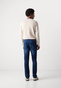 Helles beiges Langarmhemd, dunkelblaue Slim-Fit-Jeans und beige Sneakers mit braunen Sohlen. Glatter Stoff und schlichte Designdetails.