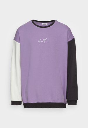 Sweat-shirt à manches longues col rond avec corps lavande, manche gauche blanche, manche droite et ourlet noirs, avec le texte « Your Turn » sur la poitrine.