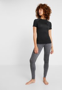 Black athletic short-sleeve top with textured shoulders paired with gray leggings featuring stripe patterns along the legs. Barefoot stance.