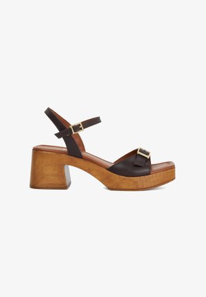 Bruine leren platform sandalen met een stevige houten hak, voorzien van verstelbare straps en accenten in goudkleurige gespen. Open teen ontwerp.