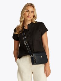 Navy leather crossbody bag with gold hardware, zippered compartment, and adjustable strap, featuring a logo on the front.