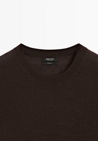 Pull en laine brun foncé avec un col rond. Le tissu est lisse avec une texture subtile. Comprend une étiquette indiquant "100 % laine".