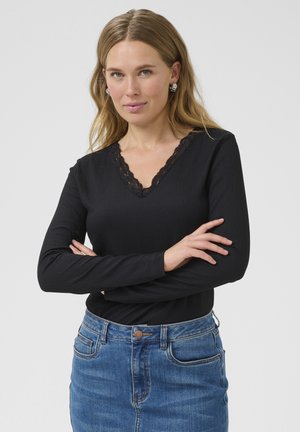 Black long-sleeve top with a V-neck and lace trim, paired with a blue denim skirt featuring front pockets and a button closure.