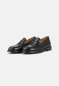 Mocassins en cuir noir avec une finition lisse, bout rond, détail de bande décorative et petit talon. Design classique adapté aux environnements formels.
