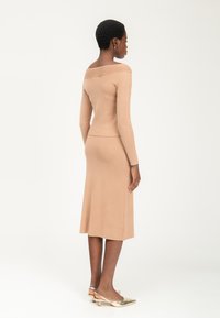 Langærmet, tætsiddende strikket kjole i beige med off-the-shoulder design og ribbede detaljer, parret med metalliske lavhælede sko.