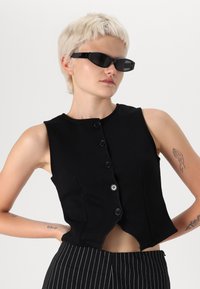 Μαύρη αμάνικη μπλούζα με στρογγυλή λαιμόκοψη, πέντε κουμπιά και καμπυλωτή γραμμή στριφώματος. Το ύφασμα είναι λείο με εφαρμοστή σχεδίαση.