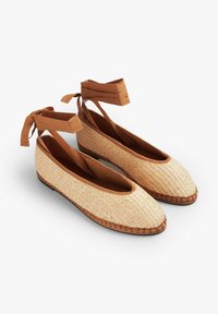 Scarpe flat in stile espadrille con tomaia in paglia intrecciata, lacci in tessuto marrone alla caviglia e una finitura marrone cucita. Rivestimento interno liscio e punta arrotondata.