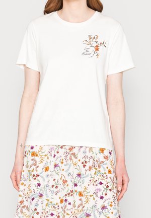 Camiseta de algodón blanca de mangas cortas, con un diseño floral y el texto "Vive el Momento" impreso en marrón oscuro.