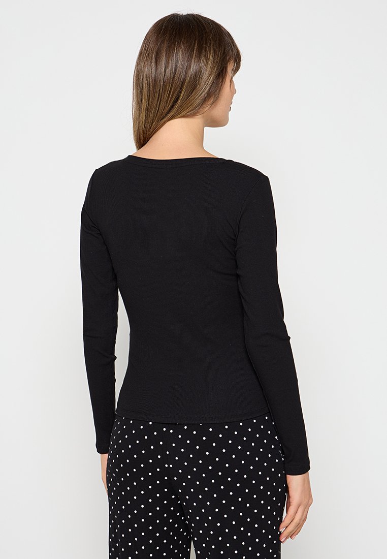 Czarny, długi rękaw bluzka z prążkowanej tkaniny z okrągłym dekoltem, w połączeniu z czarnymi spodniami w kropki. Skupienie na prostym, dopasowanym kroju.