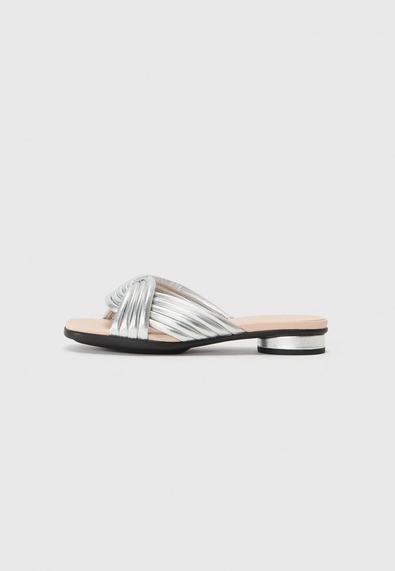 Silverfärgad metallisk slidesandal med vriden remdesign, låg blockklack och beige innersula. Svartsula som ger kontrast.