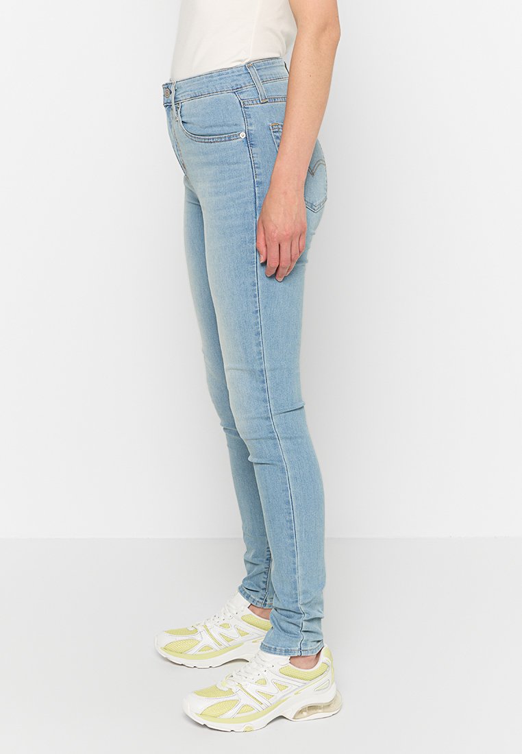 Vaqueros ajustados de color azul claro, fabricados en denim de textura suave; cuentan con presillas para cinturón y bolsillos frontales. Combinados con zapatillas blancas.