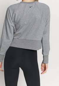 Sweatshirt gris coupe courte avec des manches raglan, des poignets côtelés et une taille élastique. Présente un petit logo Nike noir à l'arrière.