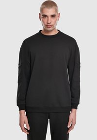 Melnā flīsa džemperis no mīkstas auduma, ar apaļu kakla izgriezumu, garām piedurknēm, ribveida aprocēm un kabatu ar rāvējslēdzēju kreisajā rokassvārstā.