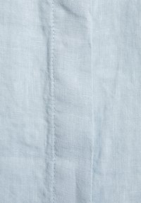 Ljusblått linne tyg med en subtil textur och synlig sömn längs sömmen, vilket skapar ett naturligt, mjukt utseende.