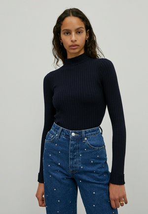 Marineblauer gerippter Rollkragenpullover mit langen Ärmeln, kombiniert mit hochtaillierten blauen Jeans aus Denim mit silbernen Nietenakzenten.