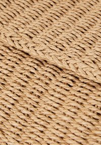 Přírodní tkaný slámový materiál v světle béžové barvě, s texturovaným, pleteným vzorem a překrývajícími se prameny pro větší hloubku.