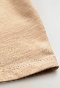 Beige tyg med en slät textur och en rullad fåll. Materialet verkar vara lätt med subtila färgvariationer.
