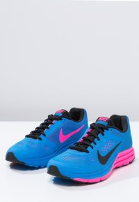 Modré sportovní boty s prodyšným síťovým svrškem, který má černé akcenty a růžový klín. Silná růžová podrážka a černé tkaničky dotvářejí design.