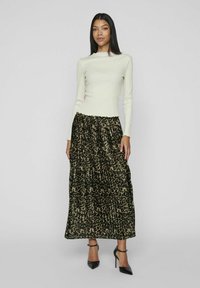 Elfenbensfarvet stribet langærmet top med en bølget udskæring, parret med en lagdelt maxi-nederdel i sort og beige leopardmønster. Sorte højhælede sko.