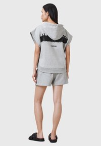 Sweatshirt gris avec capuche, manches courtes, et un design graphique noir au dos. Associé à un short assorti et des sandales noires.