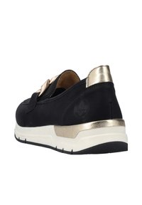 Scarpa in suede nera con un accento metallico dorato sul tacco e un dettaglio a fiocco. La suola bianca offre un design sportivo, con battistrada testurizzato nero.