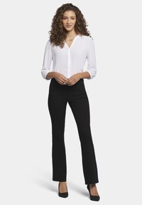 Blusa blanca con escote en V y mangas acampanadas, combinada con pantalones negros de cintura alta y tacones negros. Tejido suave, diseño sencillo.