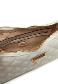 Interno della borsa crema trapuntata con fodera beige. Dotata di una tasca con zip e di una placca con logo dorato. Chiusura con zip dorata e accessori in ottone.