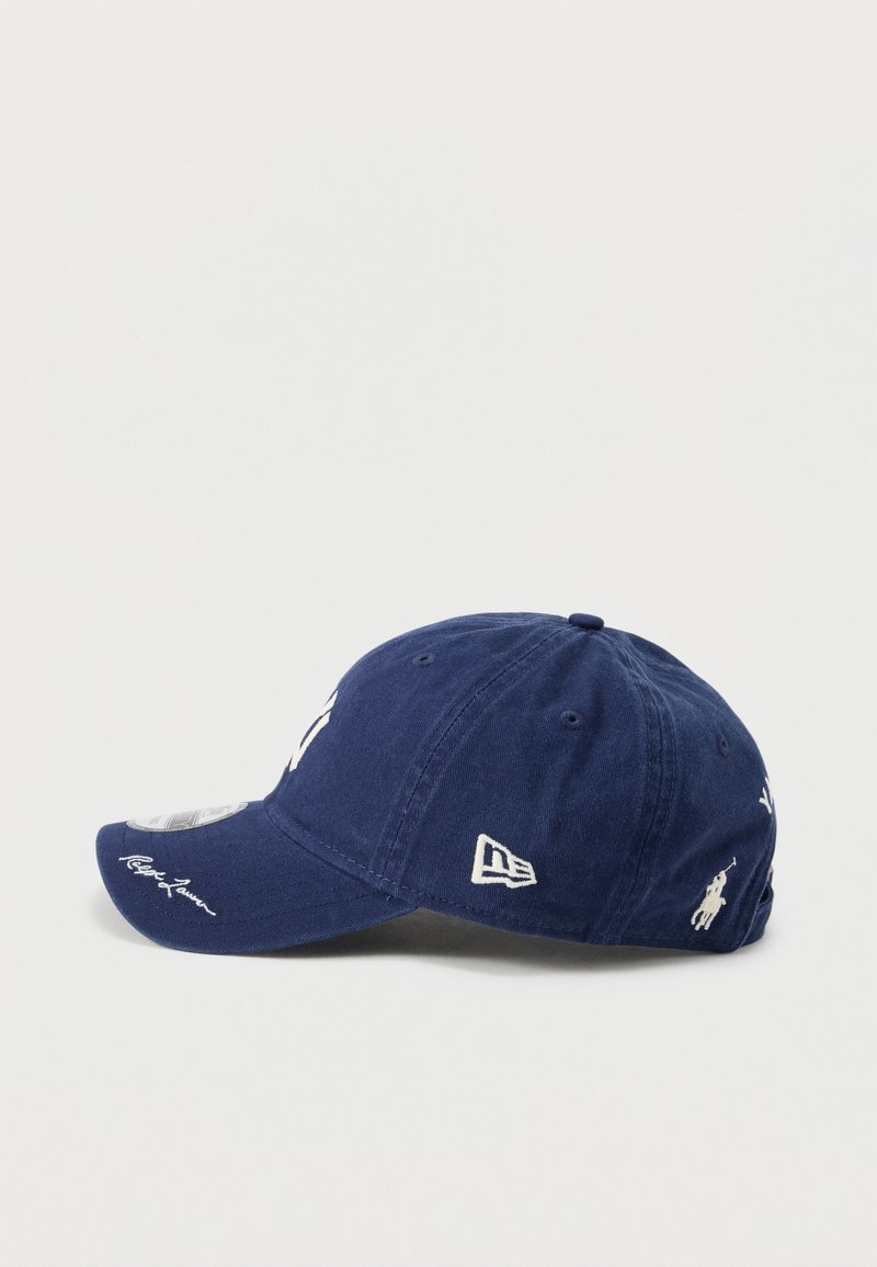Casquette de baseball bleu marine avec logos brodés blancs, dont Polo Ralph Lauren et New Era, vue de profil sur fond blanc.