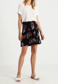 Černá květinová sukně s růžovými a modrými květy, kombinovaná s bílým topem s krátkým rukávem a bílými nazouvacími sandály. Sukně má sklady.