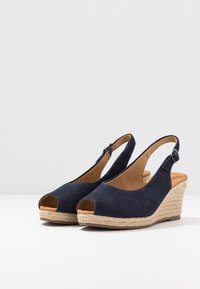 Námořnické modré semišové klínové sandály s otevřenou špičkou, juty obalené klíny, design se slingback a nastavitelným popruhem na kotníku. Hladká vnitřn�í podšívka.