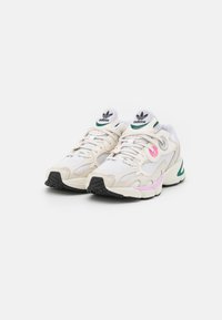 Vita sneakers med nät och syntetiska material. Har rosa och gröna accenter, svarta gummisålar och en logotyp på tungan.