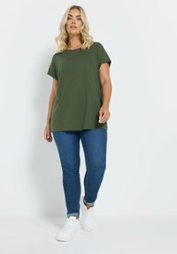 Oliven grøn kortærmet t-shirt med en afslappet pasform, parret med blå denim skinny jeans og hvide sneakers. Glat stoftekstur.