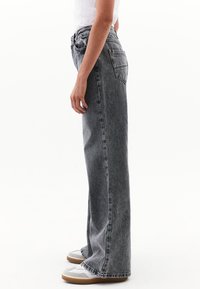 Vaqueros de denim gris con cintura alta, corte amplio, cinco bolsillos y dobladillo deshilachado. Se llevan con zapatillas gris y blanco.