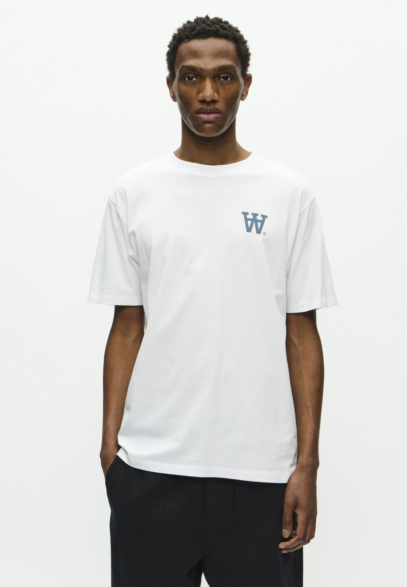 Weißes Baumwoll-T-Shirt mit rundem Halsausschnitt, kurzen Ärmeln und einem blauen Logo auf der linken Brust. Schlichte, klassische Schnittform mit glatter Textur.