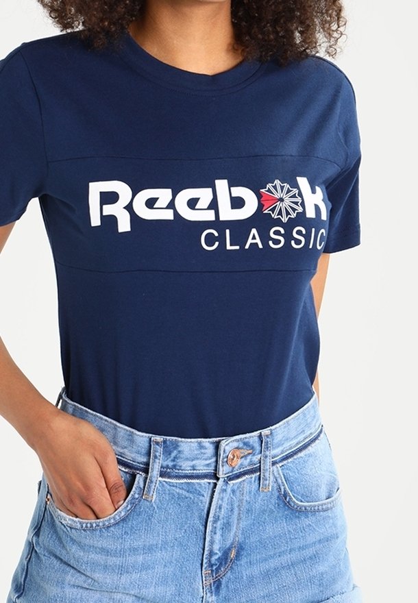 Námořnická modrá bavlněná tričko s bílým a červeným logem "Reebok CLASSIC". Krátké rukávy, kulatý výstřih, volný střih, s hladkou texturou.