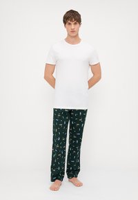 Tricou alb cu guler rotund asortat cu pantaloni de pijama verzi, ce au un imprimeu colorat cu băuturi. Materialul pare moale și ușor.